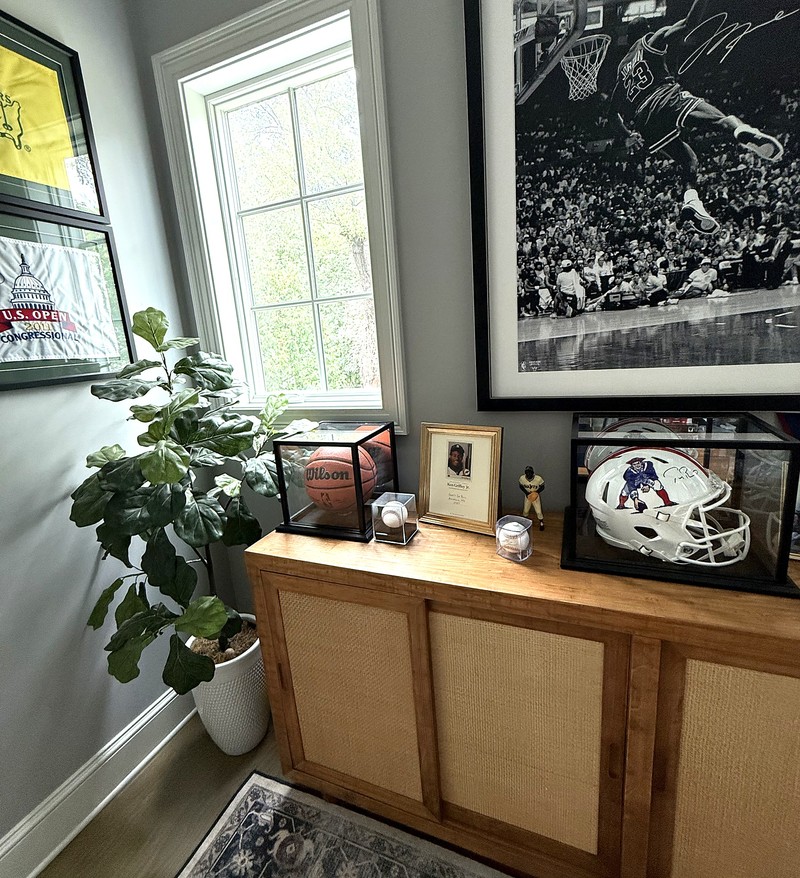 A collection in a room: framed memorabilia, signed balls in cases, and a small framed card print on a sideboard