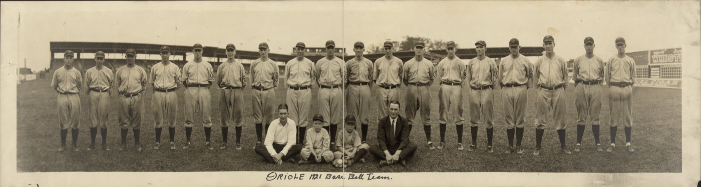 Panoramic photograph of the 1921 Baltimore Orioles, twenty players standing in uniform across a ballpark outfield with two men in street clothes and two boys seated in front